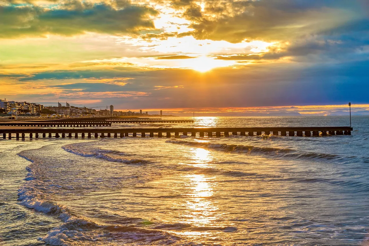 Stunning golden sunset over Jesolo beach with sunlight reflecting on the Adriatic Sea waters and a wooden pier stretching into the horizon